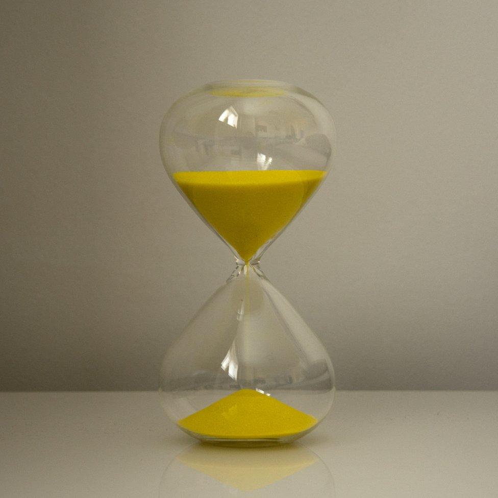 An image of a large hourglass with yellow sand inside