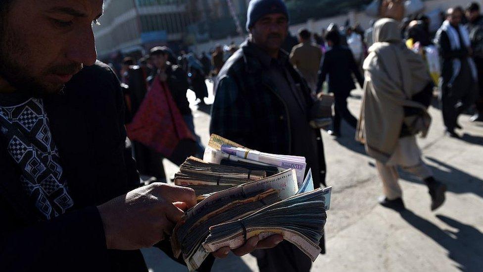 An Afghan money changer counts Afghani currency notes at the roadside in Kabul