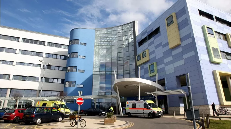 A general view picture of the John Radcliffe Hospital in Oxford, with two ambulances waiting outside, along with two cars and a few bikes chained to railings.