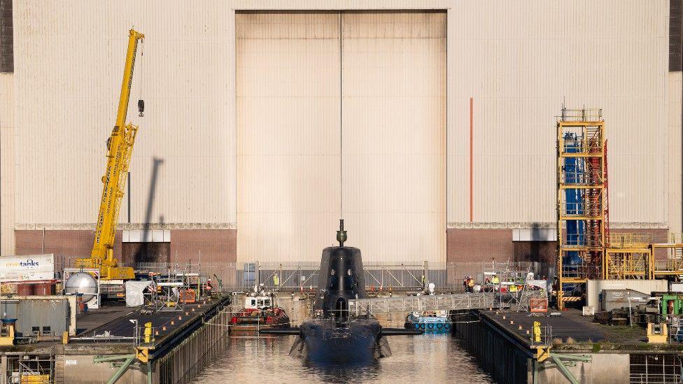 Front-on view of BAE hangar with HMS Agamemnon while it is being hoisted into the water.