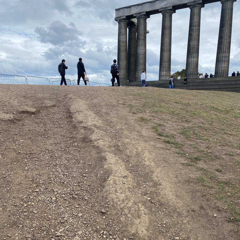Dry exposed earth and patchy grass in front of the National Monument. 