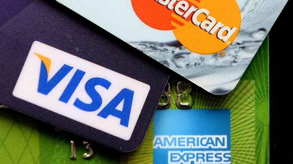 A close-up of a MasterCard credit card, a wallet that says Visa, and the American Express logo.