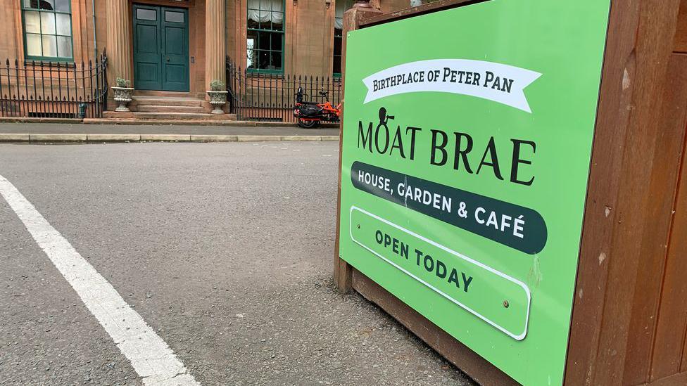 A sign for the Moat Brae visitor centre describing it as the birthplace of Peter Pan sits outside the doorway of a sandstone building