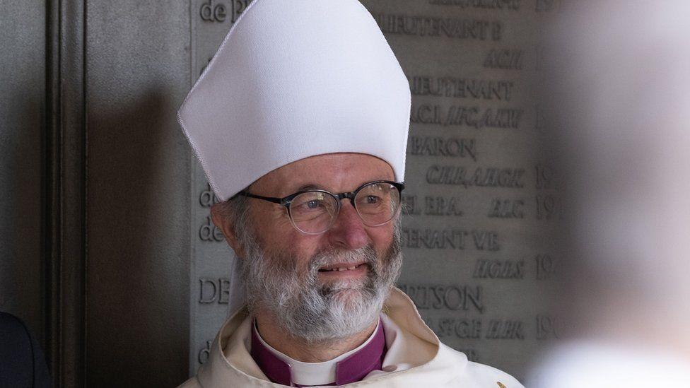 The previous bishop, the Right Reverend Dr Alan Wilson, has a white beard and glasses. He is dressed in a full bishop outfit.