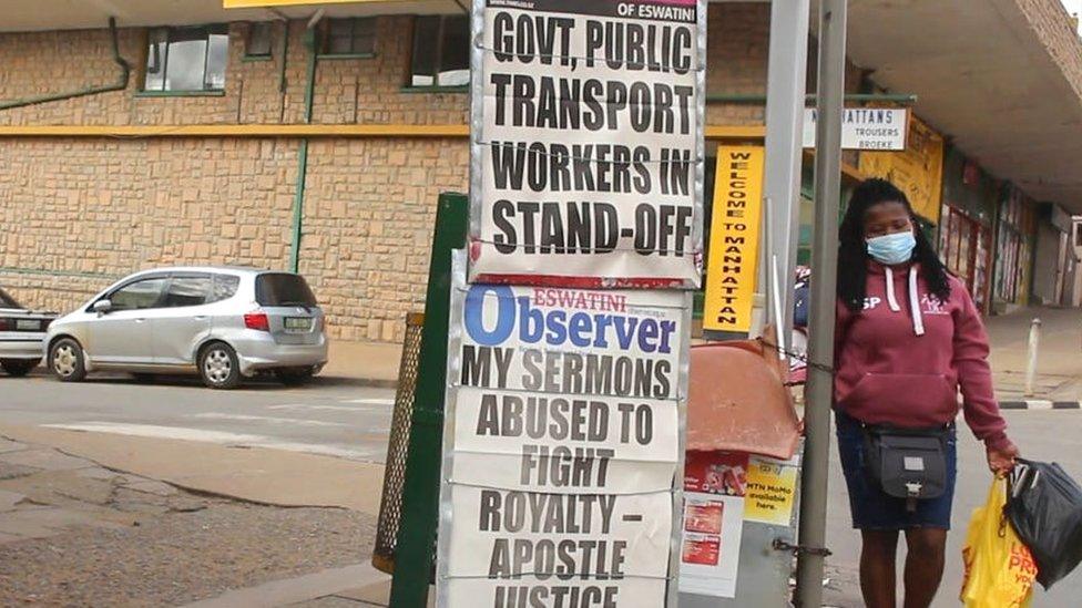 Woman walking past posters of newspaper headlines in Manzini, October 2021.