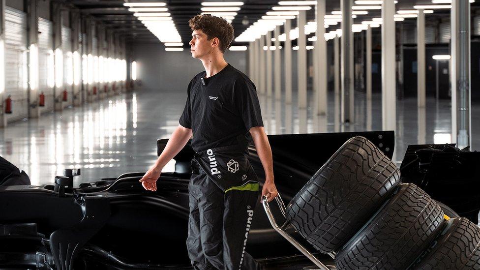 Alex Witty in a large warehouse-style space in front of a Formula One car as he pulled old tyres behind him