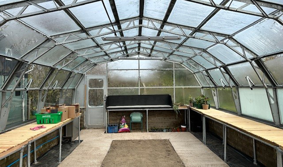 The interior of a large empty greenhouse with wooden tables down either side