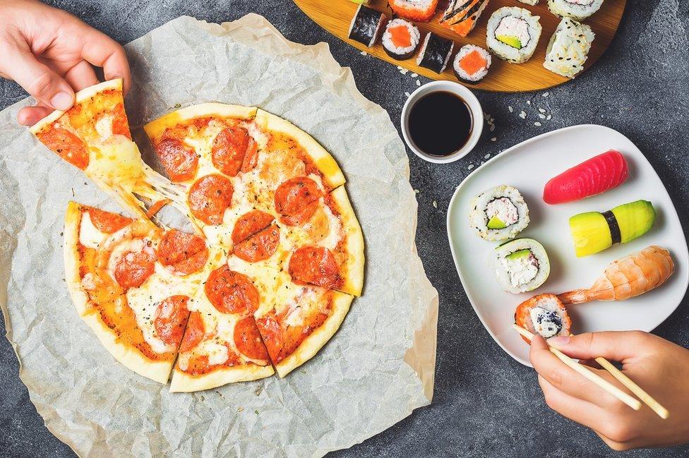 A man eating pizza while a woman has sushi