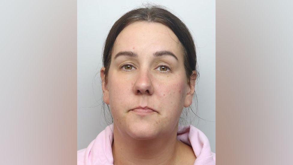 A custody photo of Lucy Connolly. She is facing the camera without an expression on her face. Her dark hair is tied back and she is wearing a light pink hoodie.