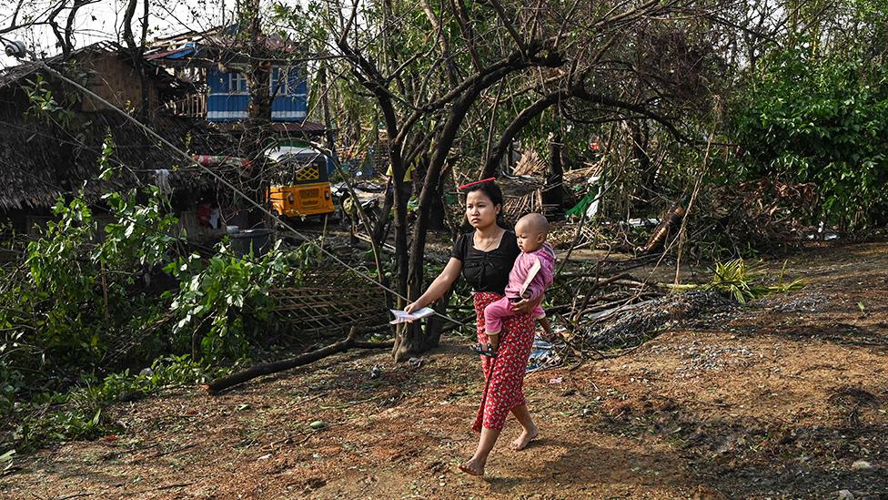 Woman carries baby as she walks past ruins of her village in Myanmar after Cyclone Mocha