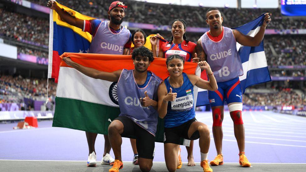 Simran and Abhay kneeling, holding the Indian flag behind them, having come third in the 200m in Paris. Behind them are the pairs who came first and second with their national flags. 