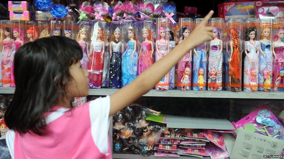 A young girl looking at pink doll packaging