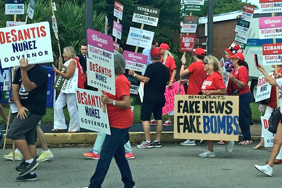 Protester with placard reading "Fake News Fame Bombs"