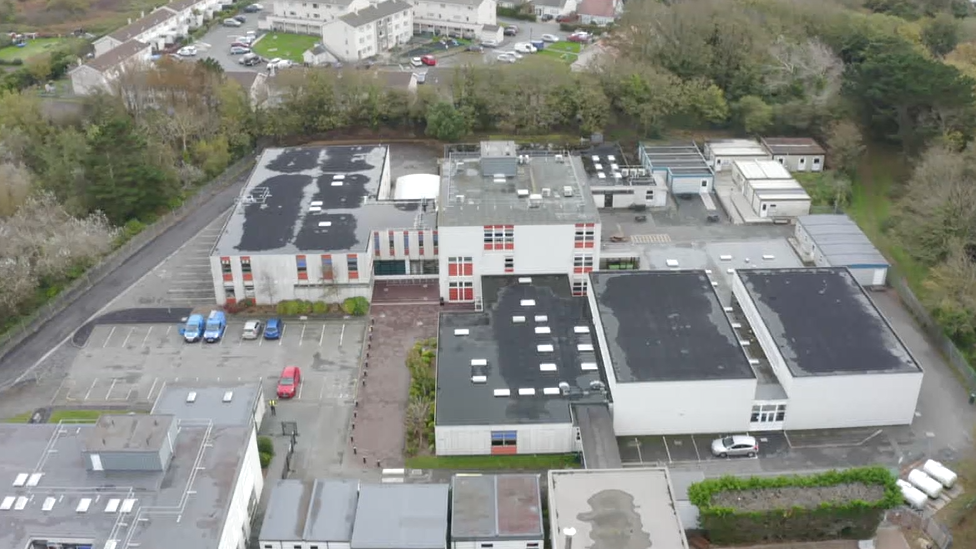 An aerial view of La Mare de Carteret High School which has a car park to its left and flat roofed buildings.