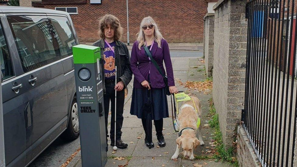 Rachael Andrewsd (right) with her husband Darryl, who has a white walking cane and her guide dog.