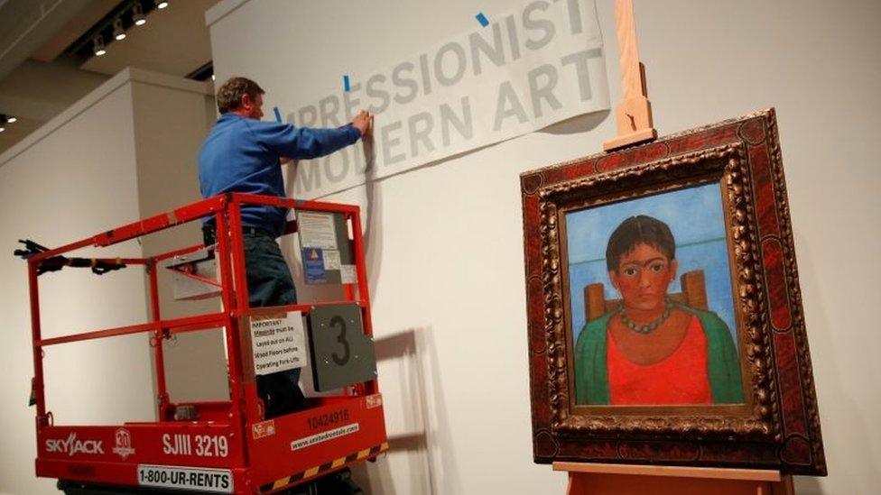 A man hangs a sign as artist Frida Kahlo's painting "Nina Con Collar" sits on an easel at Sotheby's auction house in New York U.S., November 14, 2016.