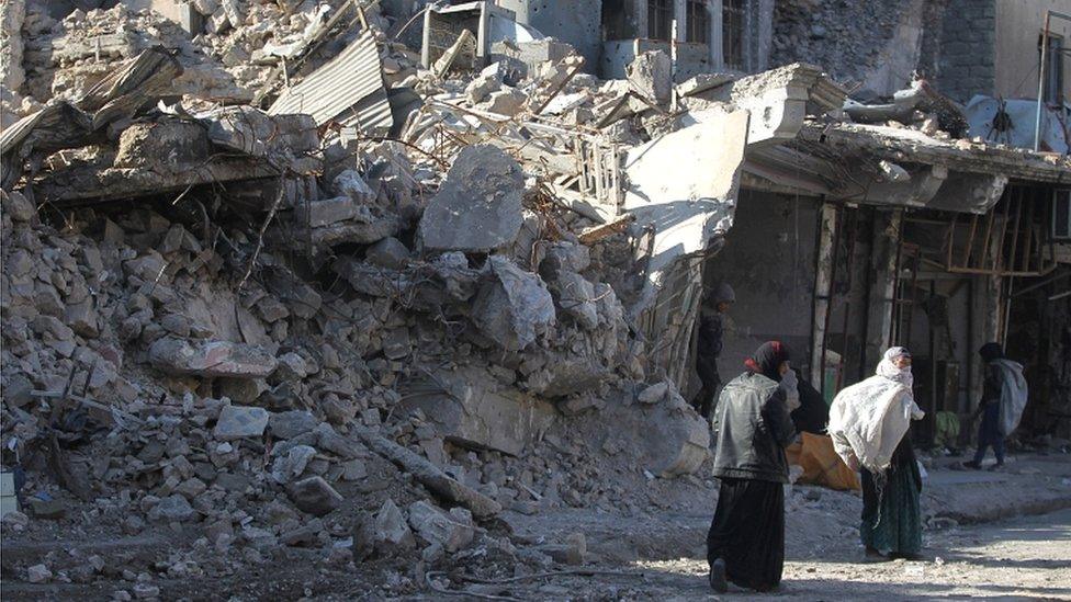 Iraqi women and children walk in the streets of the old city of Mosul to collect copper from ruins to sell and make some money, on 9 January 2018