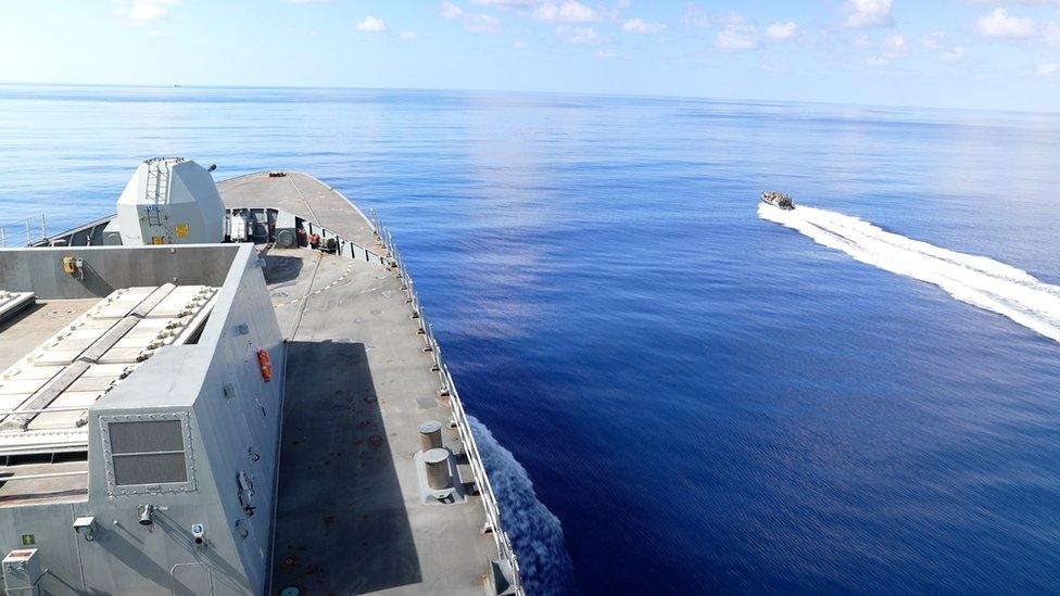 HMS Diamond is seen at sea with boat leaving to board dhow