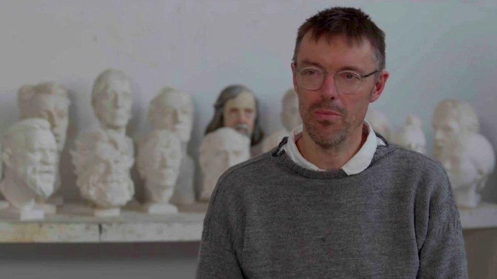 Sculptor sat in front of sculpted heads