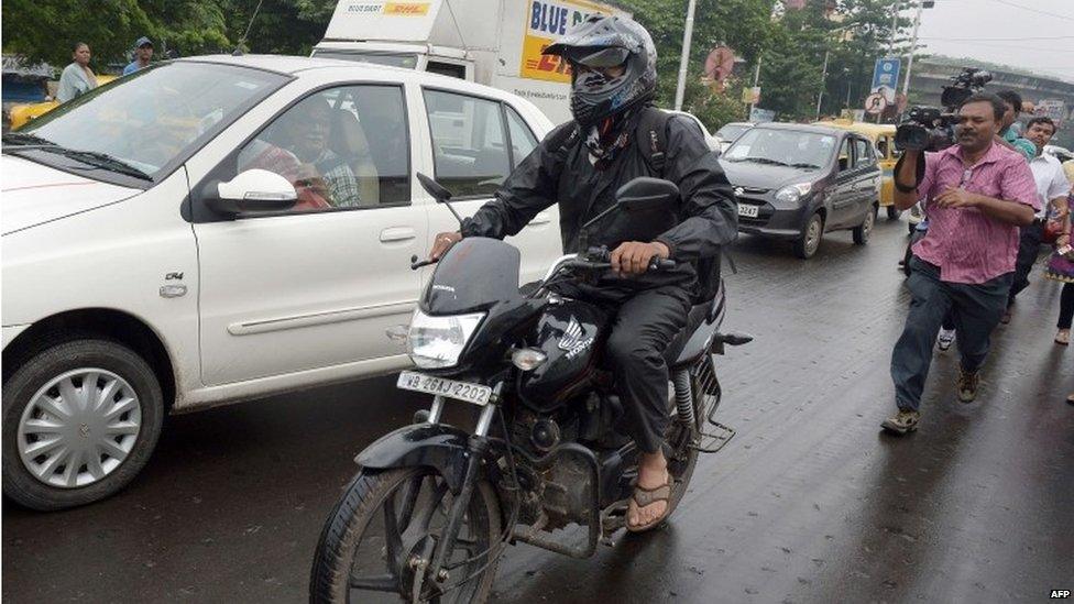 Indian man, Siddharth Das (L) tries to avoid the media as he travels on his motor-cycle on a busy road in Kolkata on September 1, 2015.