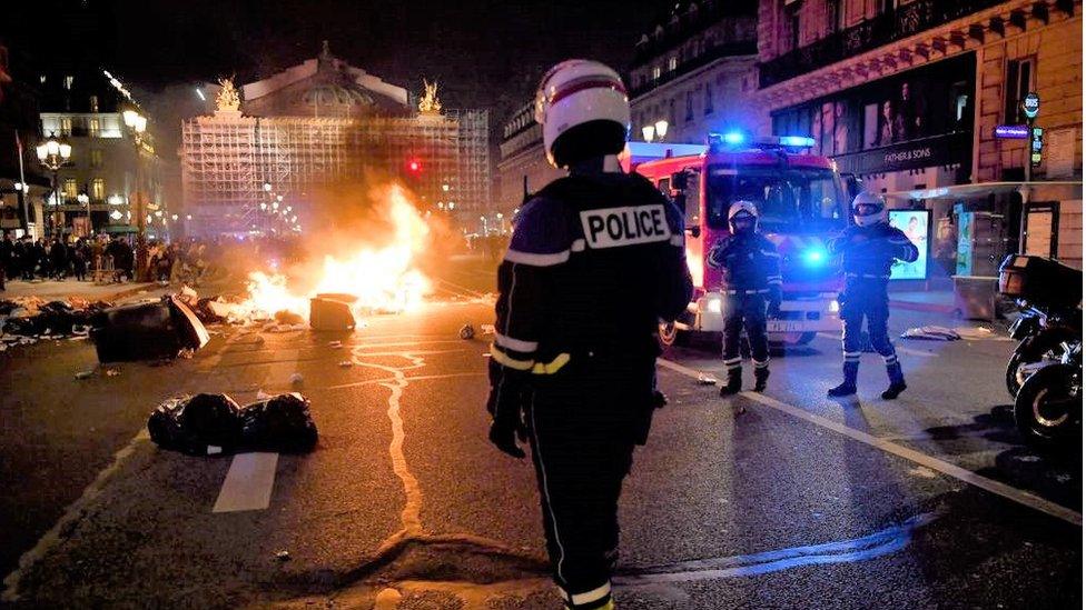 A policeman stands next to a burning pile of rubbish in front of Opera Garnier in Paris