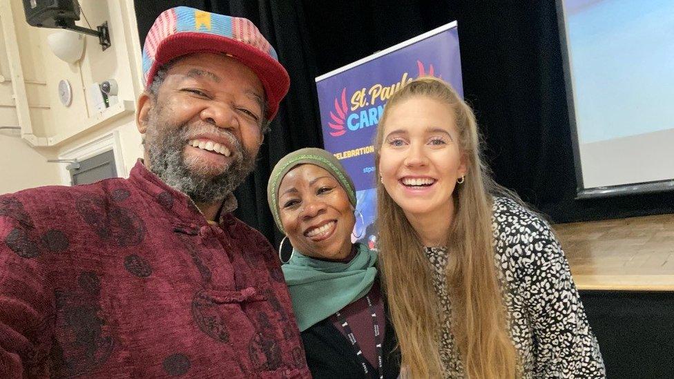 A man with a brightly coloured hat, a woman with a head scarf and a blonde woman smiling at the camera