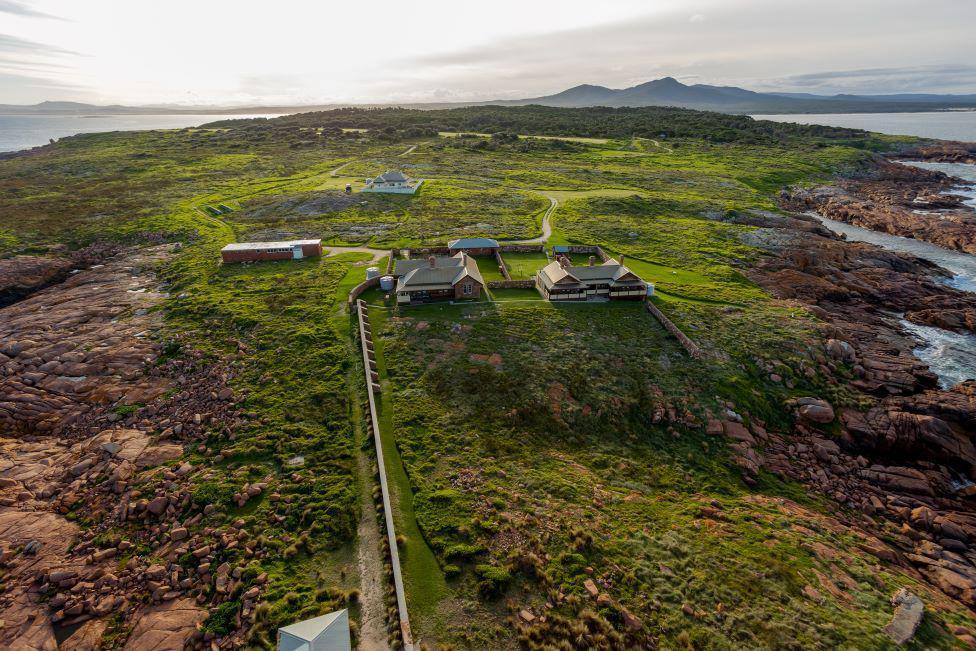 Aerial photo of small Gabo Island, with buildings visible, grassy, rocky shoreline, and see and land in the distance.