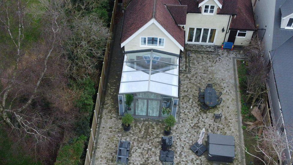 An aerial shot of the home showing the conservatory in which they were found dead and the garden, which has a large brick patio, a hot tub and chairs.
