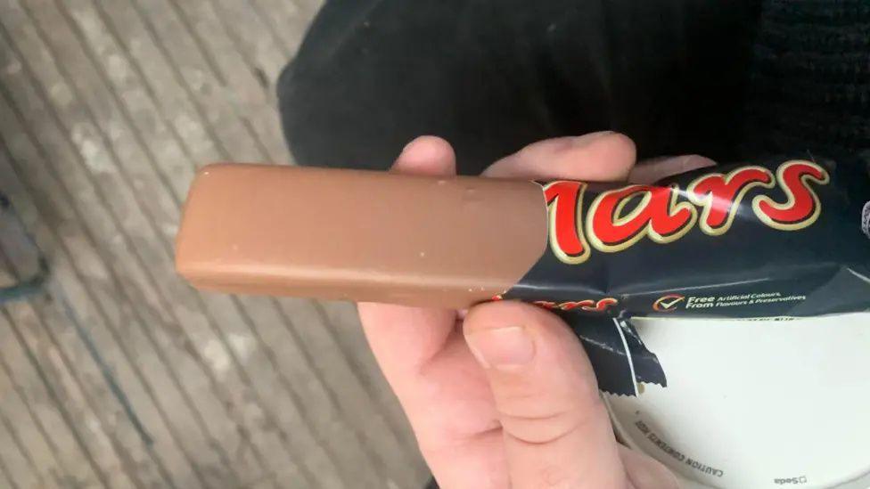 A hand holding a smooth chocolate bar in a black and red Mars wrapper.