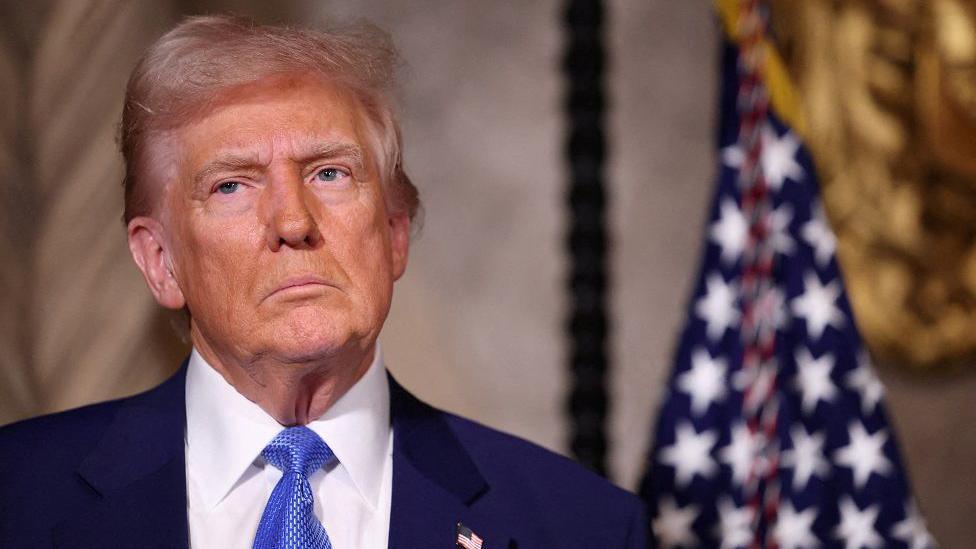 U.S. President Donald Trump looks solemn as he stands in front of an American flag at Mar a Lago in Florida