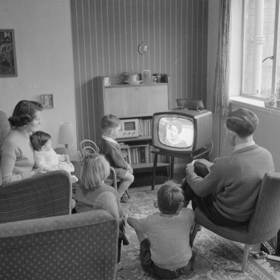 May 1958: Joan Evans watches television with her husband and four children at their new home in the new town of Harlow, Essex.