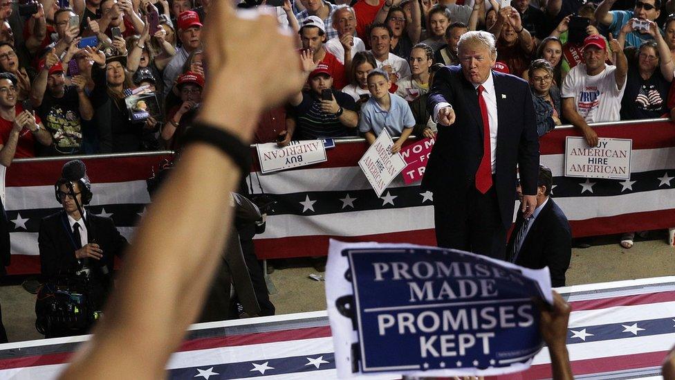 A photograph from a Trump rally shows him me pointing in direction of a supporter with a 'Promises made, promises kept' banner