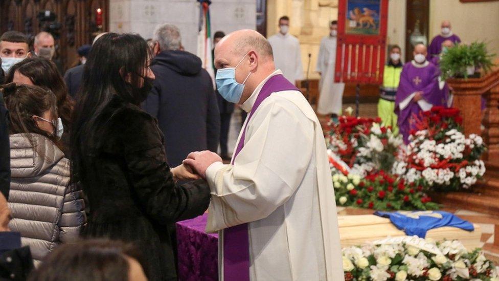 A priest comforts Rossi's widow Federica Cappelletti in front of the coffin