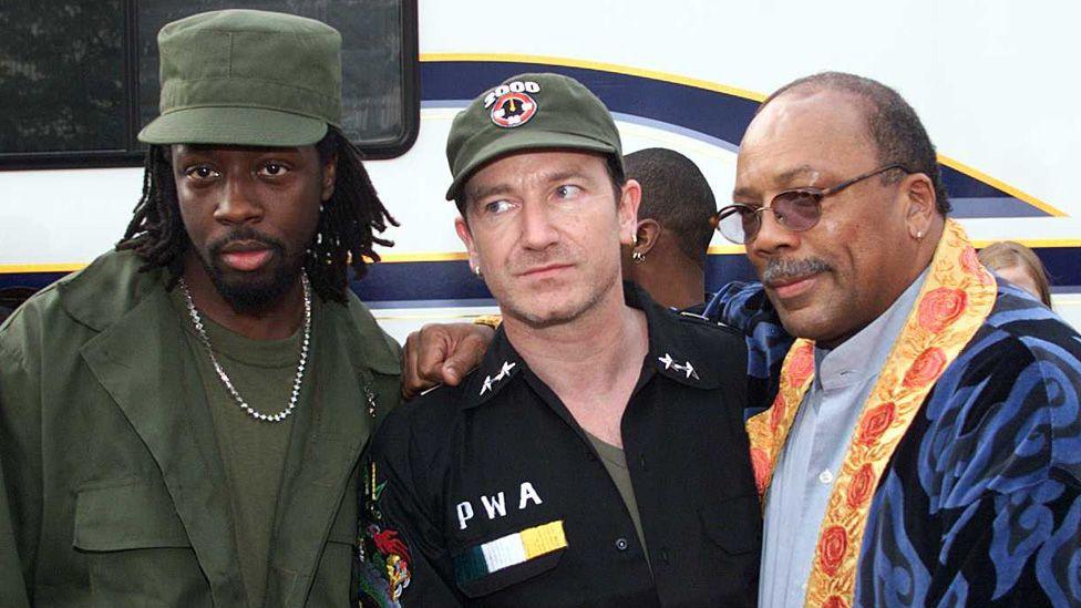 Wyclef Jean, Bono and Quincy Jones standing together outside at Net Aid at Giants Stadium in Meadowlands, New Jersey, in 1999