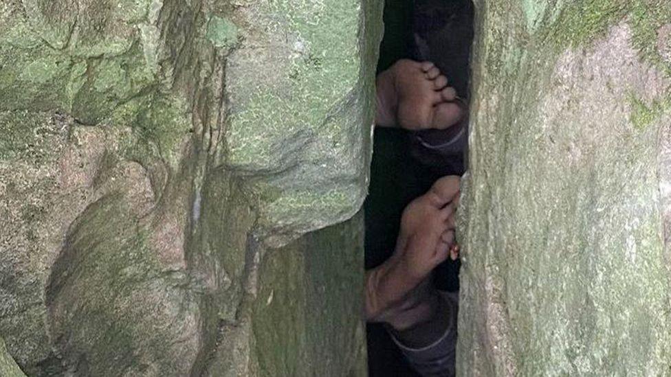 A close up of the soles of two feet trapped between two boulders