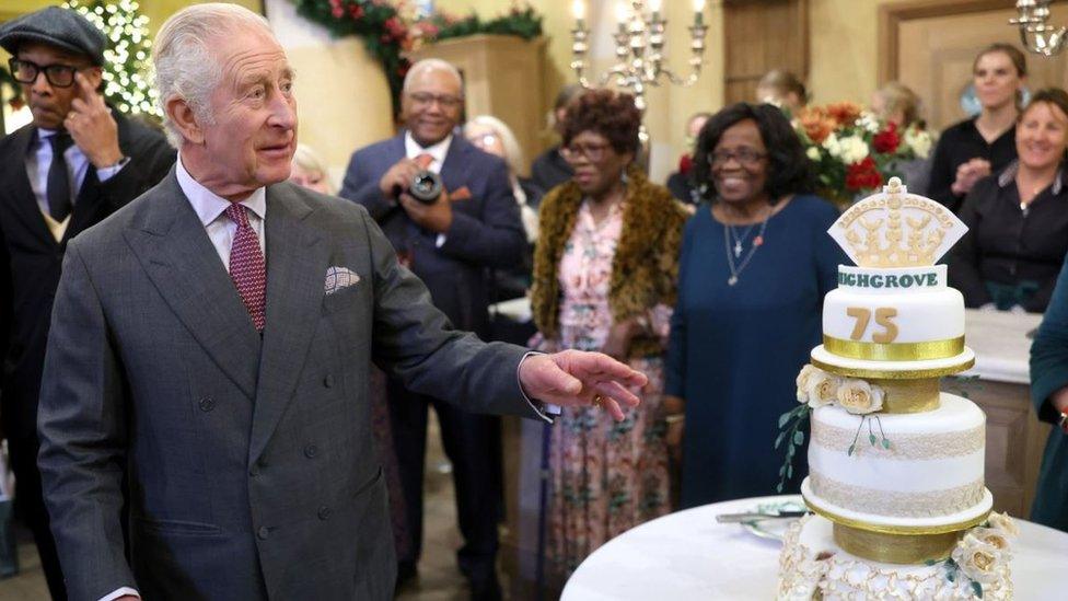 King Charles looking at a cake with guests in the background