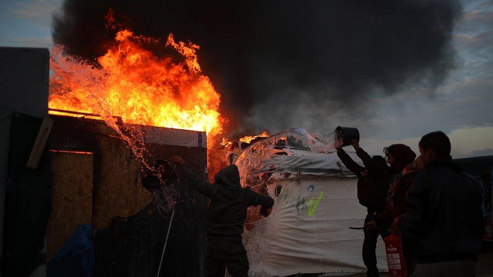 Migrants attempt to put out fire ravaging parts of the Calais refugee camp on 26 October, 2016.