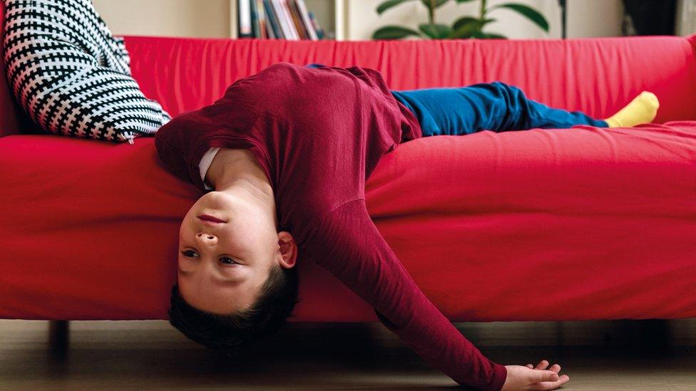 A bored-looking child lies hanging off the sofa