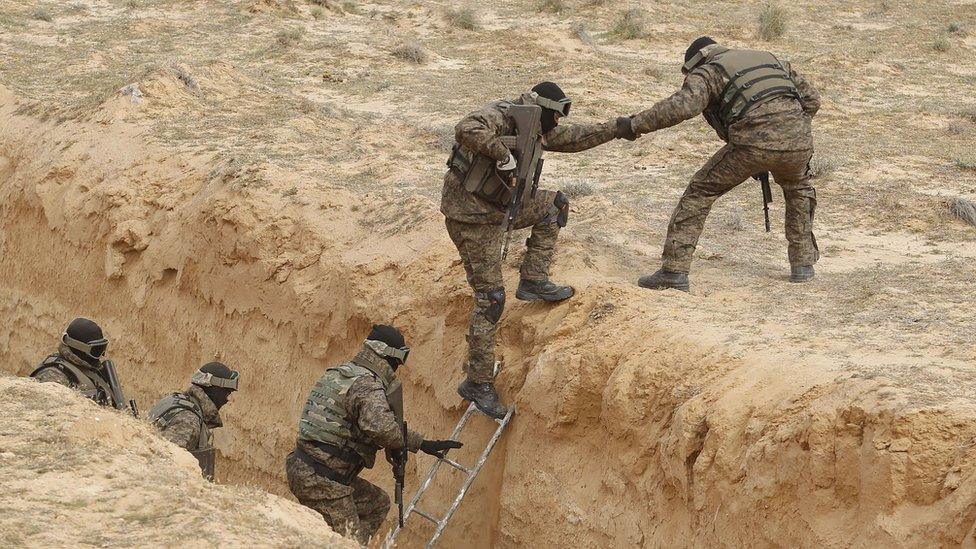 Tunisian soldiers participating in an exercise climb out of a trench, that forms part of a barrier along the frontier with Libya