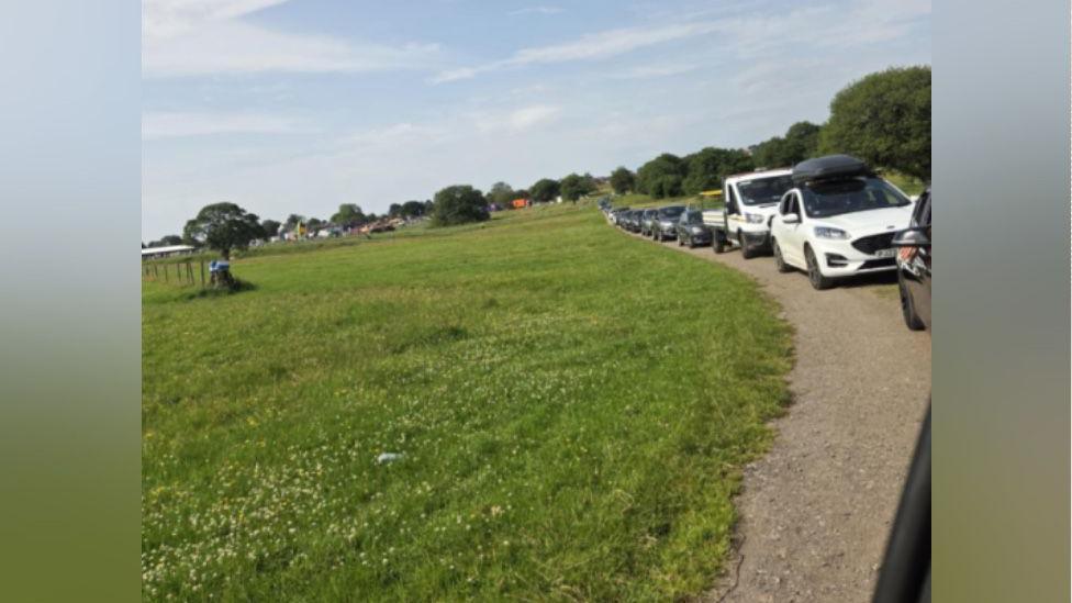 Cars are queuing up on a road in the middle of a field.