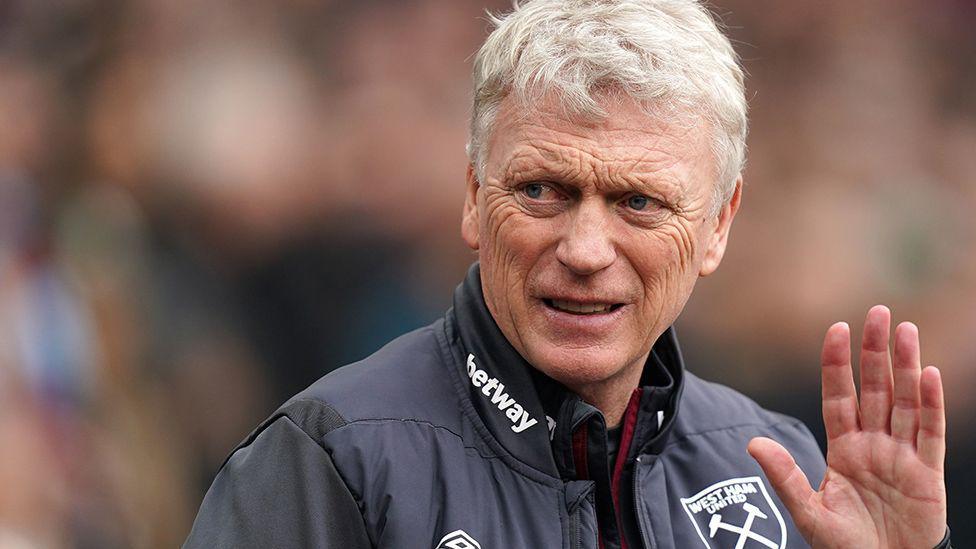  Head and shoulders image of David Moyes waving. There is a blurred crowd in the background and he has short white hair