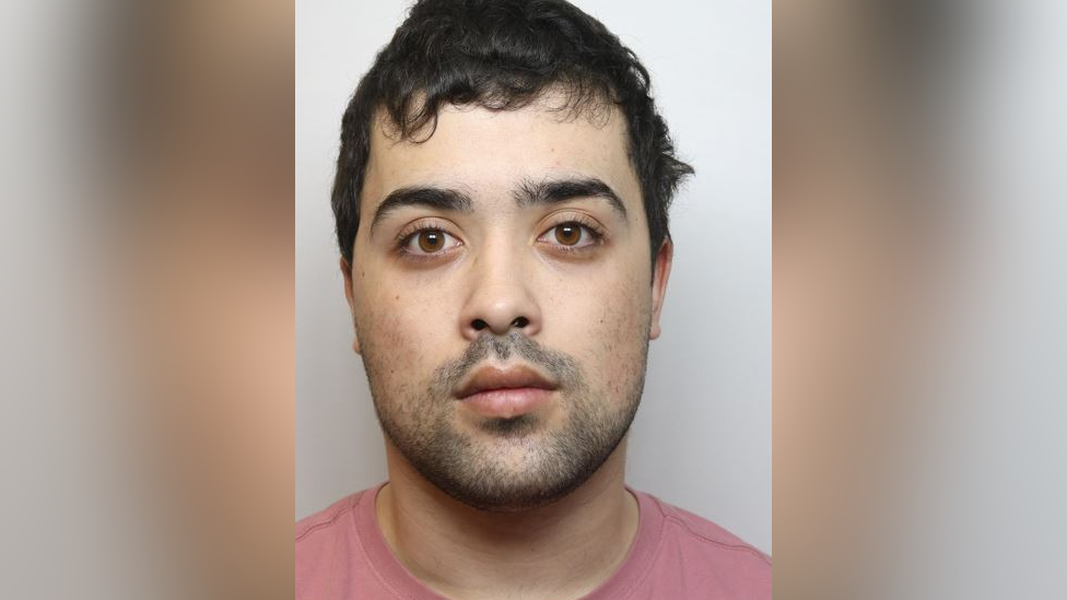 Mugshot of Damian Kinston. He has dark short hair, stubble and brown eyes. He is pictured against a plain background. He is looking directly at the camera with a blank expression. 