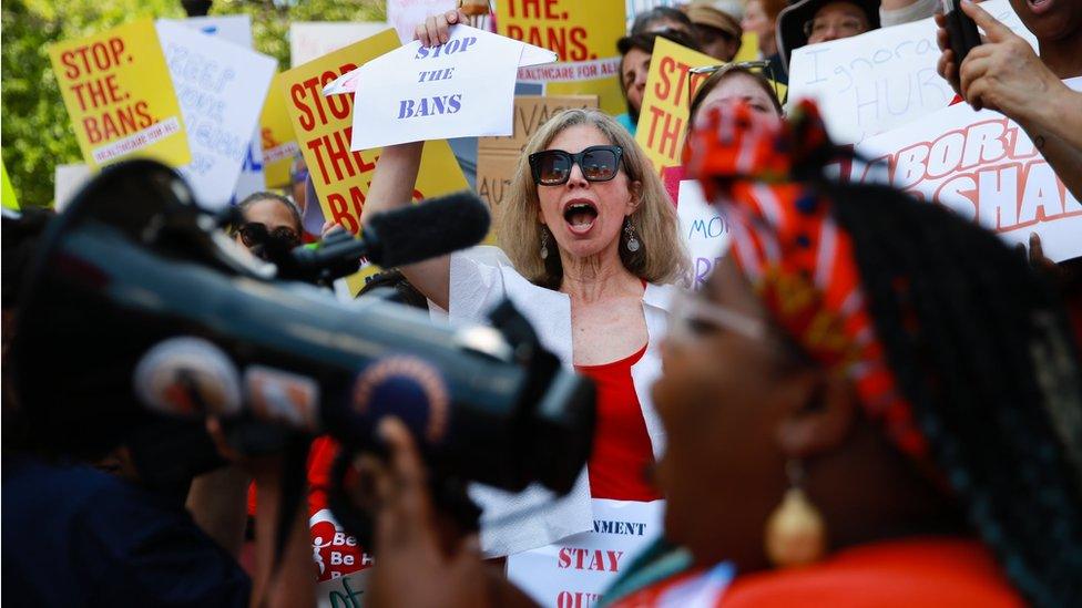 A woman holds a clothes hanger with a sign that says "stop the bans" during a protest against recently passed abortion ban bills at the Georgia State Capitol building