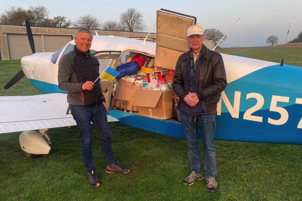 Georg Gruber (left) holds a Ukraine flag and Dick Beath (right) both standing in front of the plane which shows lot of supplies loaded on it