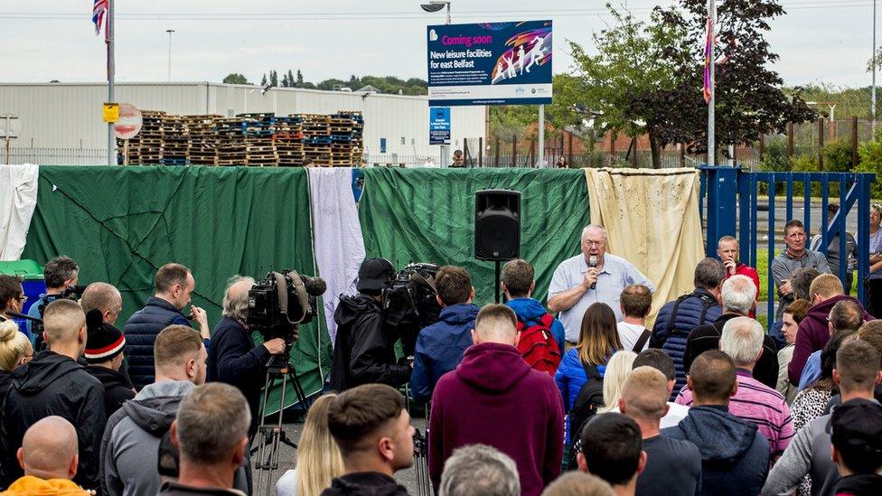 The Rev Mervyn Gibson speaks to a crowd of people at a protest at the Avoniel Leisure Centre bonfire