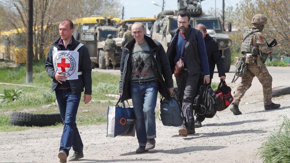 A Red Cross staff member walks with civilians who left a steel plant that was besieged by Russian forces attacking the Ukrainian city of Mariupol