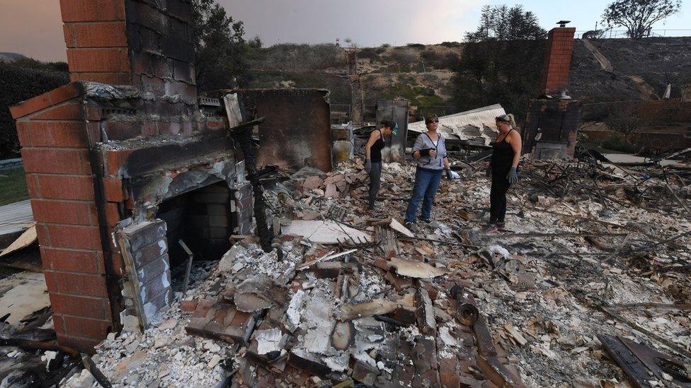 Three women stand in the burnt out shell of a house in southern California following the wildfires.