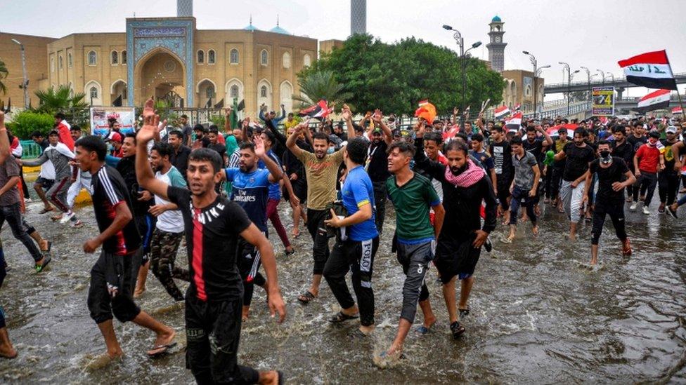 Anti-government protesters march through flood waters in the city of Najaf