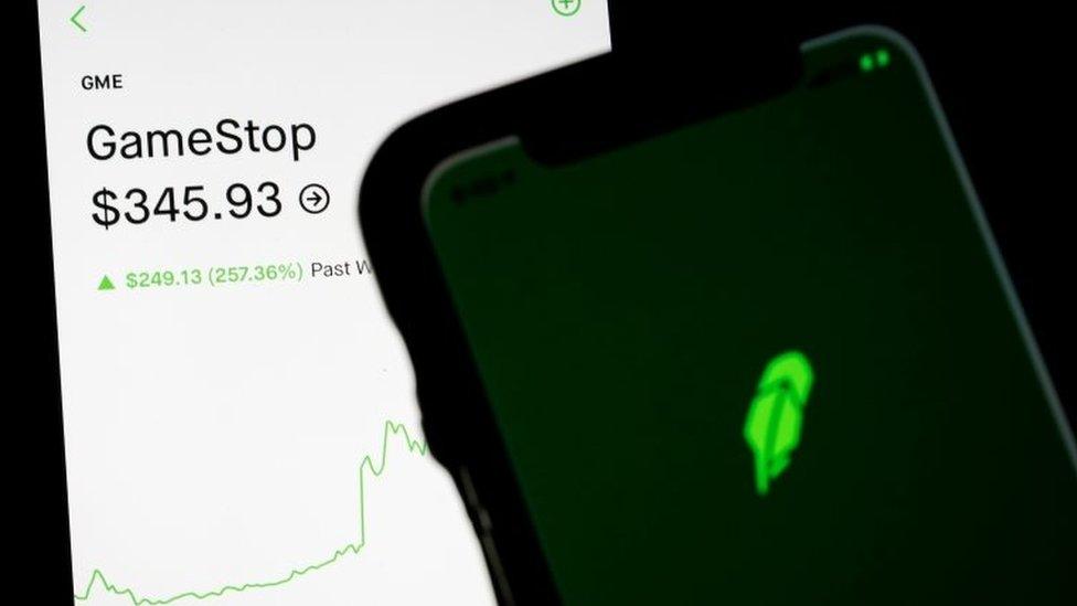 Trading information for GameStop is displayed on the Robinhood App as another screen displays the Robinhood logo in this photo illustration