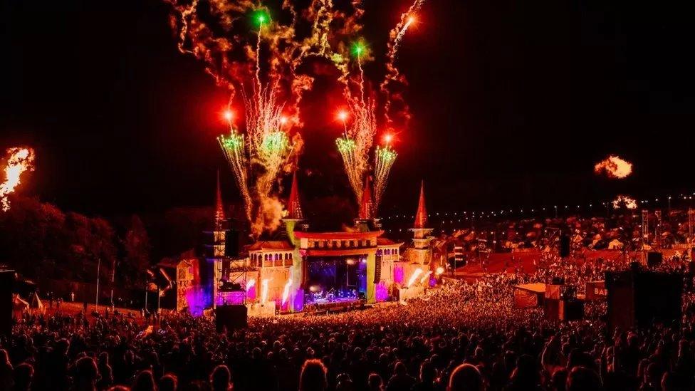 Wide shot of main Boomtown stage at night with a big crowd and fireworks coming from the stage